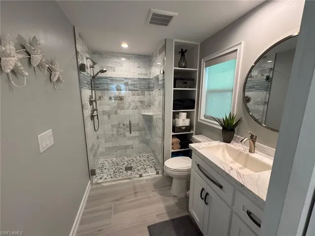 Bathroom featuring wood-type flooring, vanity, a shower with door, and toilet