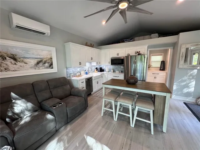 Kitchen featuring a breakfast bar, appliances with stainless steel finishes, lofted ceiling, white cabinets, and an AC wall unit