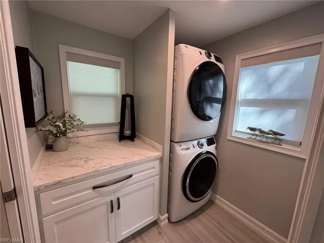 Clothes washing area with light wood-type flooring, a wealth of natural light, stacked washer and dryer, and cabinets