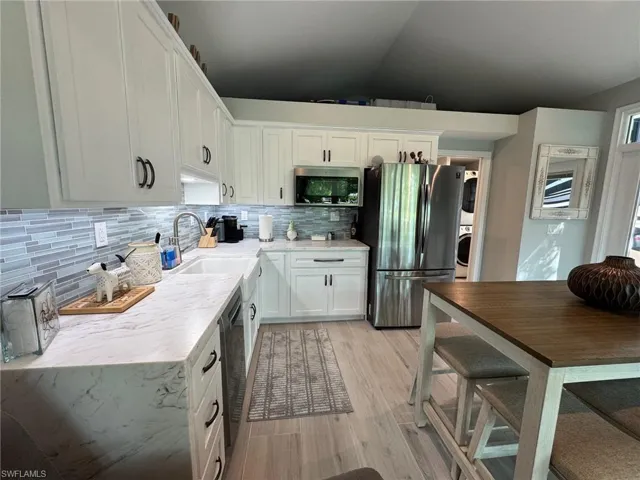 Kitchen with stainless steel appliances, vaulted ceiling, sink, white cabinetry, and light wood-type flooring