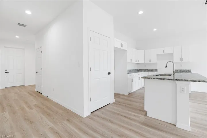 Kitchen featuring white cabinetry, stone-finish countertops, an island with a stainless steel faucet, and wood-finish flooring throughout