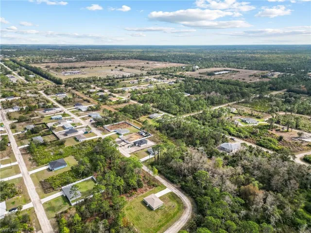 Aerial perspective of a multi-acre residential plot featuring cleared land, established tree coverage, and paved street access