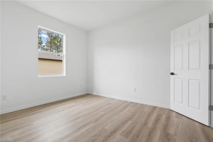 Interior space featuring wood-finish flooring, white walls, a single-hung window, and a six-panel door with matte black hardware