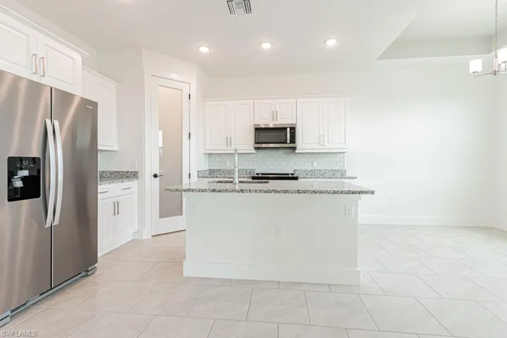 Kitchen featuring stainless steel appliances, tasteful backsplash, light stone counters, white cabinetry, and light tile patterned flooring