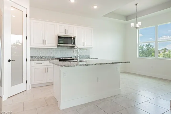 Kitchen featuring stainless steel microwave, light stone counters, tasteful backsplash, white cabinetry, and hanging light fixtures