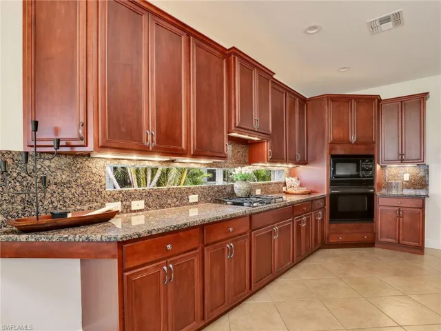 Kitchen with black appliances, stone countertops, decorative backsplash, and light tile patterned floors