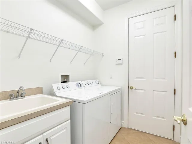 Clothes washing area featuring washing machine and clothes dryer, light tile patterned floors, cabinets, and sink
