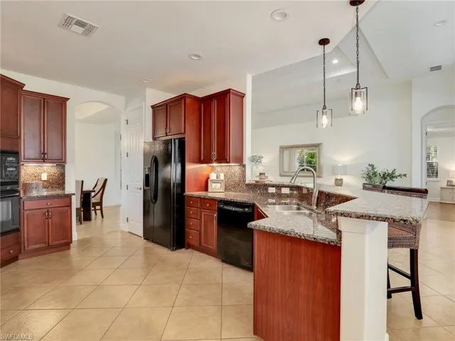 Kitchen featuring backsplash, sink, black appliances, hanging light fixtures, and a breakfast bar area