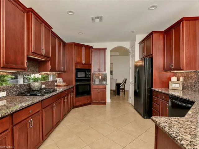 Kitchen featuring decorative backsplash, light stone countertops, light tile patterned floors, and black appliances