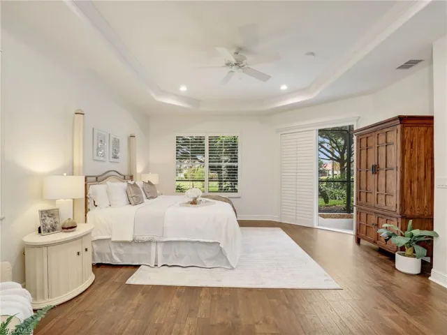Bedroom with ceiling fan, ornamental molding, dark wood-type flooring, and a tray ceiling