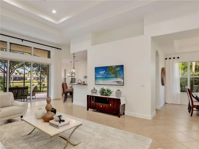 Living room with light tile patterned floors, a raised ceiling, crown molding, and a high ceiling