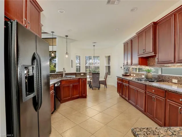 Kitchen featuring a notable chandelier, black appliances, sink, dark stone countertops, and decorative light fixtures