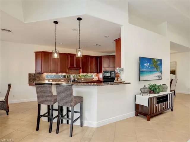 Kitchen with kitchen peninsula, backsplash, black appliances, hanging light fixtures, and a breakfast bar area
