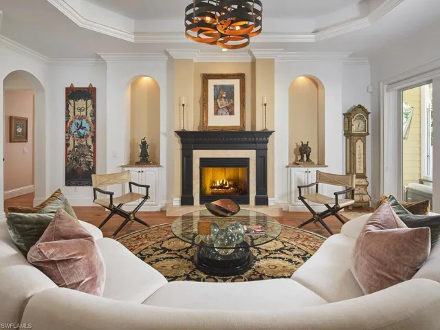 Living area featuring crown molding, a premium fireplace, arched walkways, a tray ceiling, and wood finished floors