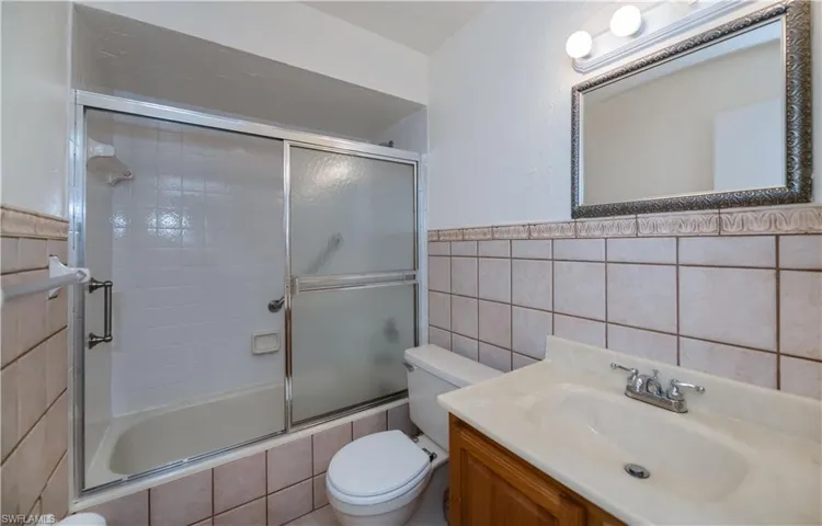 Bathroom with vanity, tile walls, and bath / shower combo with glass door