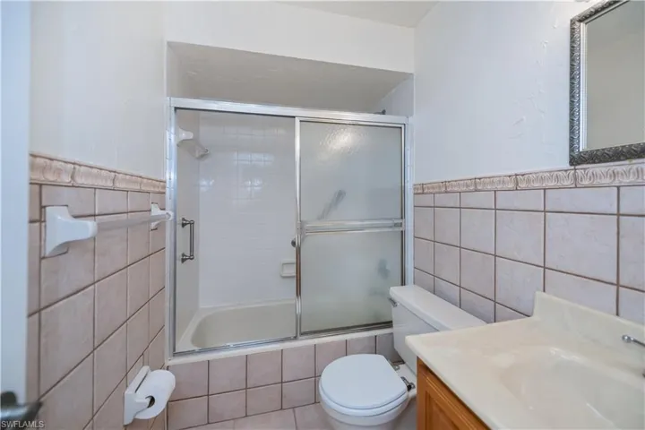 Full bath with tile walls, vanity, shower / bath combination with glass door, and a wainscoted wall