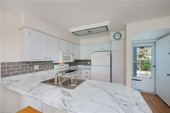 Kitchen with white appliances, light countertops, white cabinets, and decorative backsplash