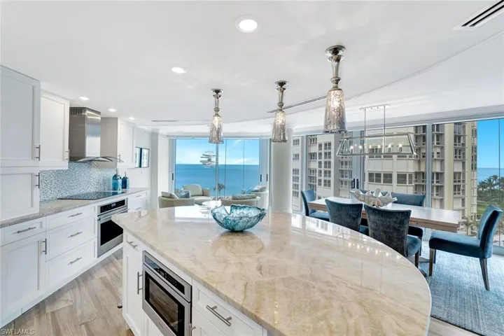 Kitchen featuring light stone countertops, wall chimney range hood, a center island, white cabinets, and stainless steel appliances