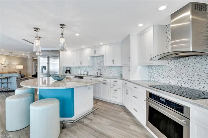 Kitchen featuring wall chimney range hood, white cabinets, appliances with stainless steel finishes, a sink, and a breakfast bar area