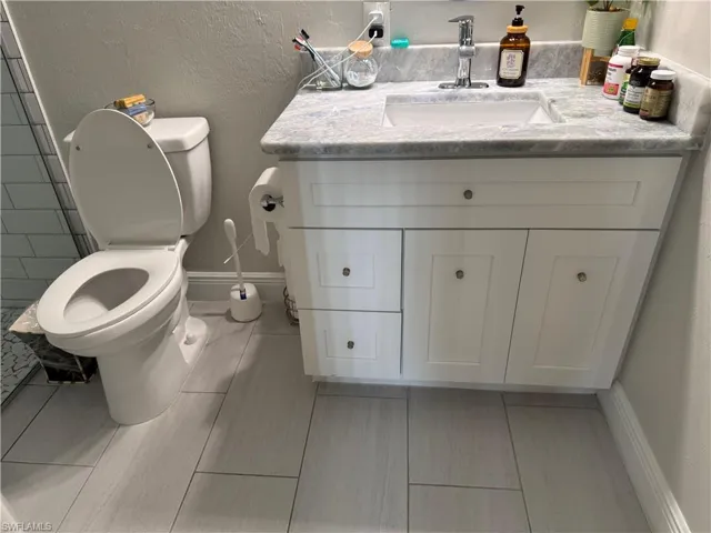 Bathroom featuring a white vanity with shaker-style cabinetry, a gray patterned countertop, an undermount sink with a chrome faucet, and rectangular tile flooring