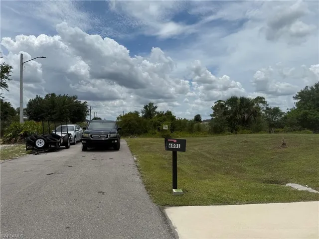 Expansive grass lot featuring a mailbox with visible numbers, paved street access, and a concrete apron