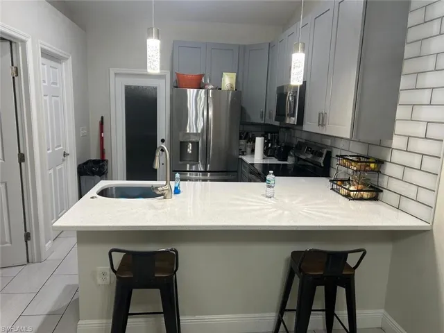 Kitchen featuring light gray cabinetry, white subway tile backsplash, stainless steel appliances, and a white countertop island with an undermount sink and gooseneck faucet
