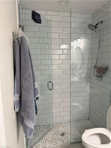 Full glass shower enclosure featuring white subway tile surround and a pebble stone shower floor