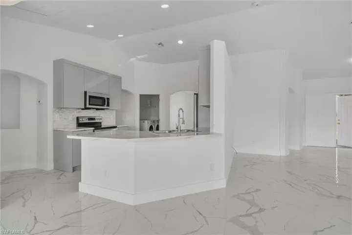 Kitchen with gray cabinetry, arched walkways, modern cabinets, a peninsula, and vaulted ceiling