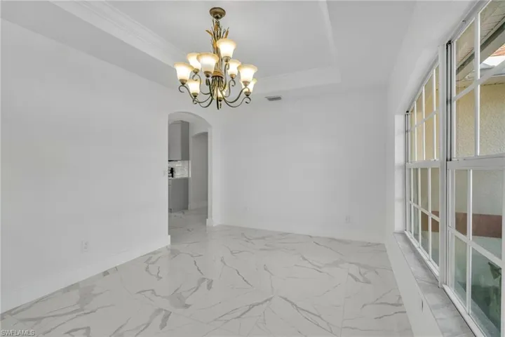 Unfurnished room featuring a chandelier, a tray ceiling, arched walkways, light marble finish floors, and crown molding