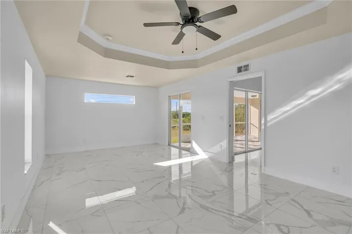 Unfurnished room with a tray ceiling, ornamental molding, light marble finish floors, and a ceiling fan