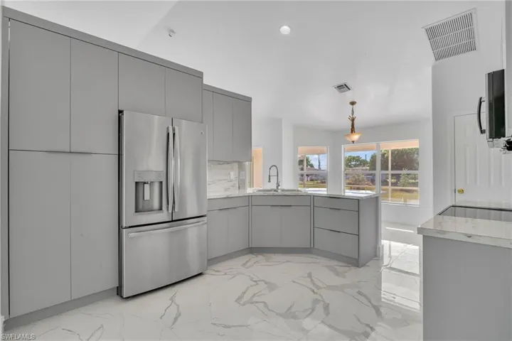 Kitchen featuring light marble finish floors, gray cabinets, stainless steel appliances, a peninsula, and modern cabinets