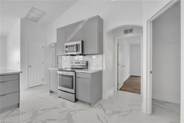 Kitchen with gray cabinets, arched walkways, light marble finish floors, and lofted ceiling