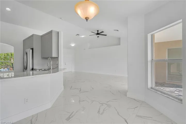Kitchen featuring gray cabinetry, light stone countertops, freestanding refrigerator, lofted ceiling, and decorative light fixtures