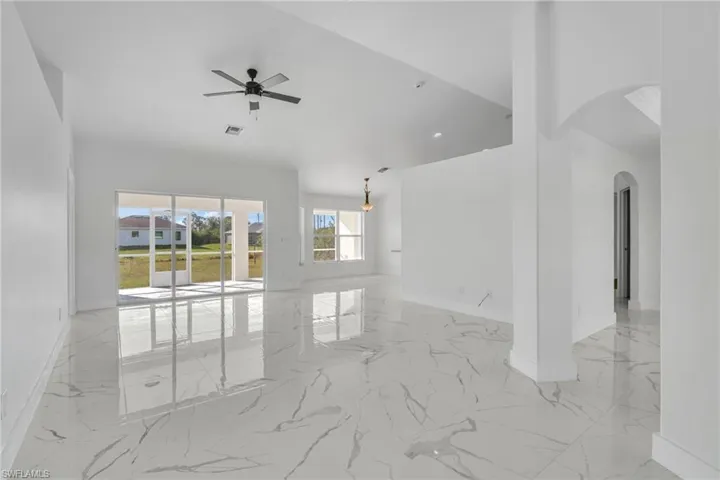 Spare room with light marble finish flooring, arched walkways, ceiling fan, and a towering ceiling