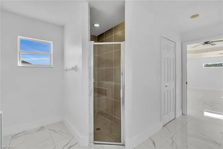 Full bathroom featuring a stall shower, ceiling fan, and light marble finish floors