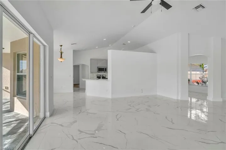 Spare room featuring arched walkways, vaulted ceiling, light marble finish flooring, and ceiling fan
