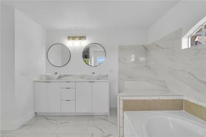 Bathroom featuring double vanity, a garden tub, and light marble finish flooring