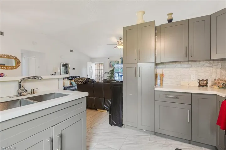 Kitchen featuring light marble finish floors, gray cabinetry, light stone counters, lofted ceiling, and open floor plan
