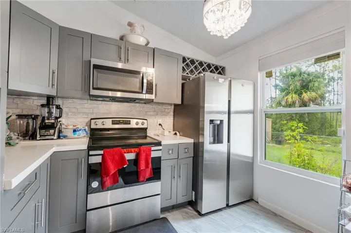 Kitchen with gray cabinets, stainless steel appliances, lofted ceiling, a chandelier, and decorative backsplash