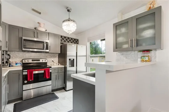 Kitchen featuring gray cabinets, appliances with stainless steel finishes, glass insert cabinets, crown molding, and tasteful backsplash