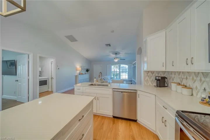 Kitchen featuring a peninsula, stainless steel appliances, white cabinets, light wood-style flooring, and vaulted ceiling