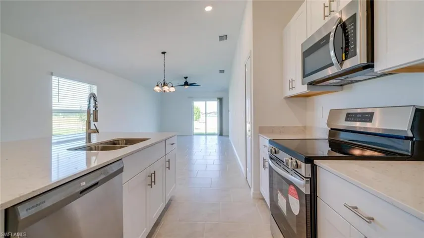 Kitchen with an inviting chandelier, light tile patterned floors, appliances with stainless steel finishes, sink, and white cabinets
