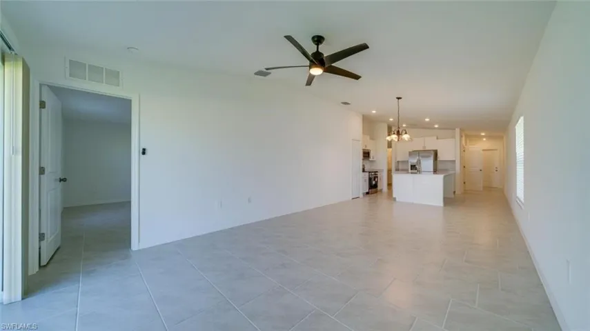 Unfurnished living room with light tile patterned floors and ceiling fan with notable chandelier