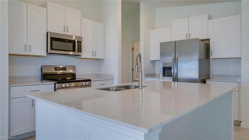 Kitchen with a kitchen island with sink, sink, stainless steel appliances, and white cabinets