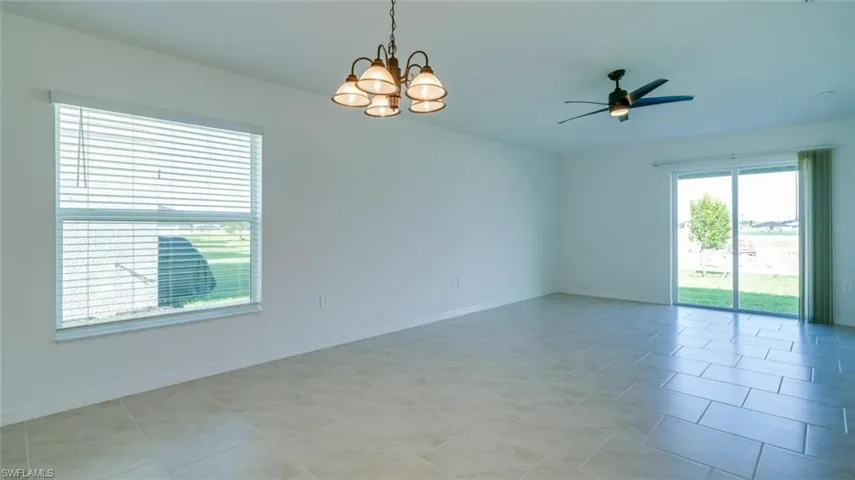 Tiled spare room with ceiling fan with notable chandelier