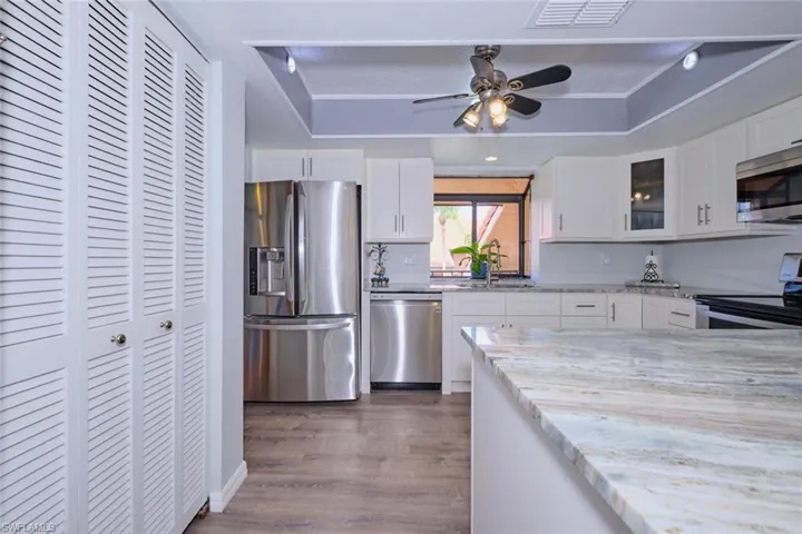Kitchen with stainless steel appliances, glass insert cabinets, light stone counters, white cabinetry, and a tray ceiling