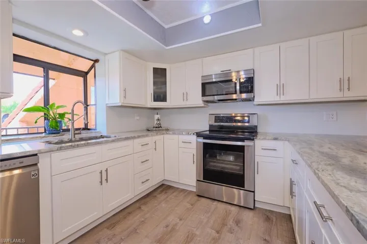 Kitchen with stainless steel appliances, white cabinets, glass fronted cabinets, and light wood-type flooring