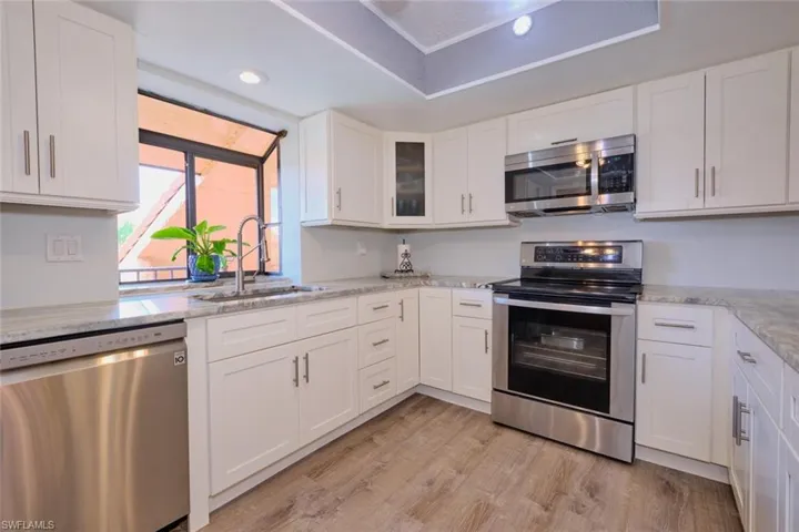Kitchen featuring stainless steel appliances, white cabinetry, glass fronted cabinets, light wood-type flooring, and light stone countertops