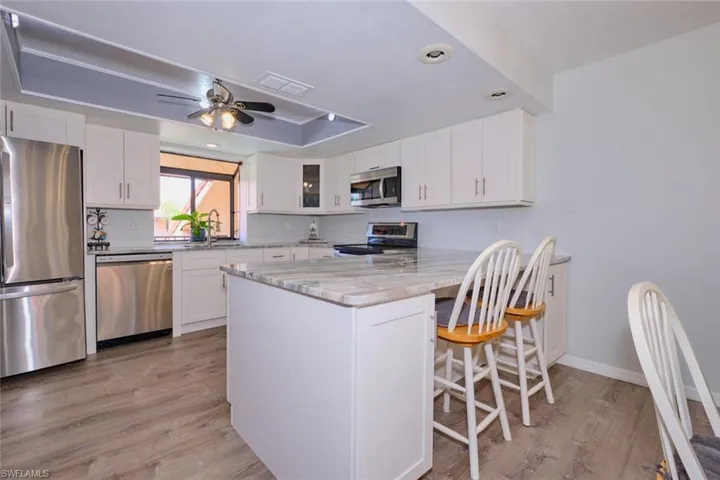 Kitchen with stainless steel appliances, a kitchen bar, light wood-type flooring, white cabinetry, and recessed lighting