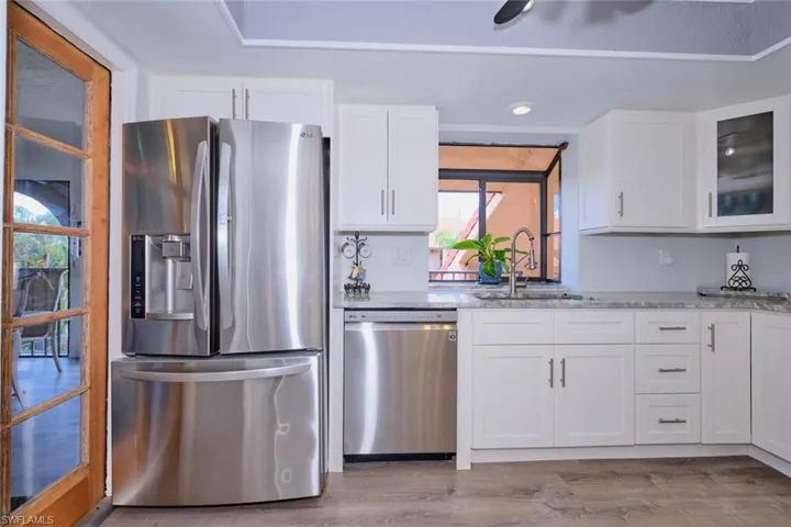 Kitchen with stainless steel appliances, white cabinets, light stone counters, and glass fronted cabinets